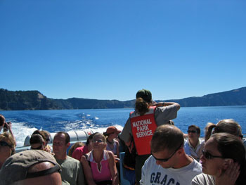 People on moving boat on Crater Lake and lady with red life saving jacket with National Park Service on it