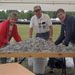 Three older people stand under a tent and over a table filled with soda can tabs
