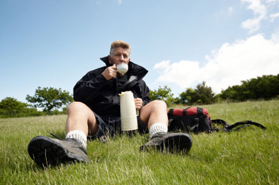 Hiker sitting in a grass field drinking from this thermos