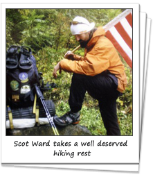 Hiker Scot Ward holds an American flag as he rests against a rock in the woods
