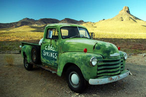 Old green truck parked on side of road with mountains in the background