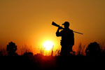 Hunter holding a rifle over his shoulder silhouetted by a setting sun