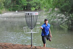 Disc golfer throws a frisbee at a basket with river behind him