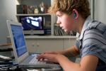 A teenage boy listens to music while using his laptop computer.