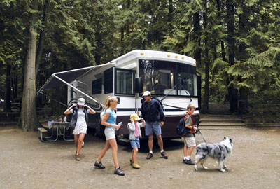 Family with their dog leaving their Class A motorhome parked at a campsite