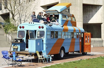 Orange and blue RV bus parked with a group of people sitting on the roof