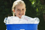 Little girl smiling and holding a blue recycling bin full of empty plastic bottles