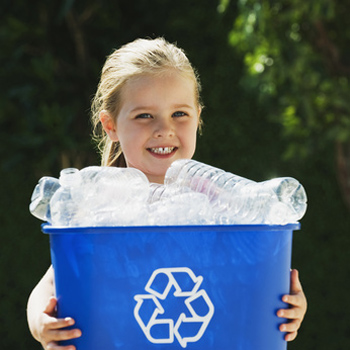 Little girl smiling and holding a blue recycling bin full of empty plastic bottles