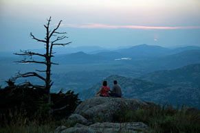 Couple sitting on top of mountain looking over the sunset view