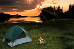 Sunset over a lake with a pitched green tent by a campfire
