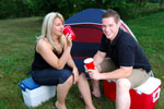 Couple drinking at a campsite sitting on coolers in front of their tent