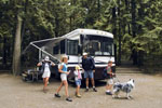 Family with their dog leaving their Class A motorhome parked at a campsite